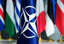 Free Riders Warned — U.S. Tab Closing NATO flag in front of various national flags