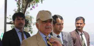 A group of men in formal attire at an outdoor event, with one man wearing a cap