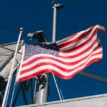 AI Lifeboat Dares Iran’s Doorstep A naval destroyer displaying the American flag and various signal flags