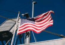 AI Lifeboat Dares Iran’s Doorstep A naval destroyer displaying the American flag and various signal flags