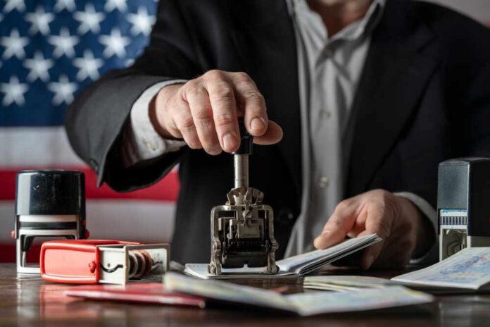 Immigration,And,Passport,Control,On,The,American,Flag,Background,,Close A person stamping passports on a desk with various stamps and documents