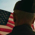 VA Warns: Fireworks Trigger Combat Flashbacks A veteran in uniform standing in front of an American flag at sunset