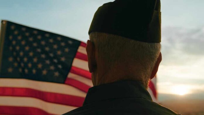 Elderly,Man,Stand,Against,American,Flag,For,Veterans,Day,Holiday A veteran in uniform standing in front of an American flag at sunset