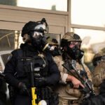 Blue States Demand No ICE Pledge Police officers in tactical gear wear gas masks during a crowd control operation