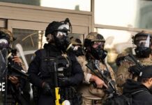 Blue States Demand No ICE Pledge Police officers in tactical gear wear gas masks during a crowd control operation