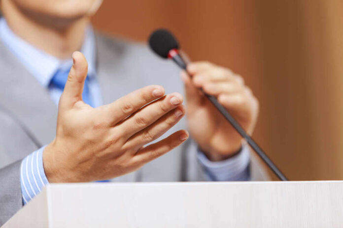 Businessman,Standing,On,Stage,And,Reporting,For,Audience Two people speaking at a podium with microphones