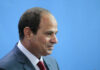 Middle East Flashpoint: Trump Meets Sisi A serious-looking man in a suit with a red tie, surrounded by blurred figures
