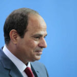 Middle East Flashpoint: Trump Meets Sisi A serious-looking man in a suit with a red tie, surrounded by blurred figures