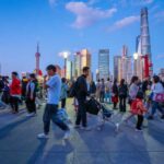 Global AI Order—Made In Shanghai? Crowd walking on a riverside promenade at dusk with modern skyline in background