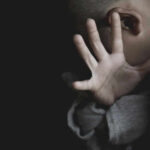 Child covering face with hand in dim light