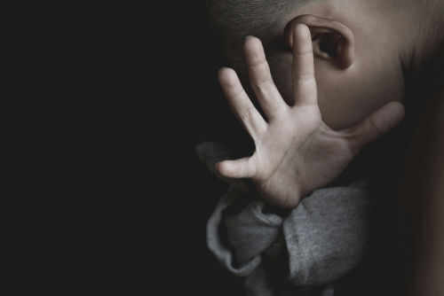 kids-abuse1183793743 Child covering face with hand in dim light