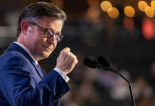 Mike Johnson Lights A Voting Firestorm Man speaking at a podium with two microphones.