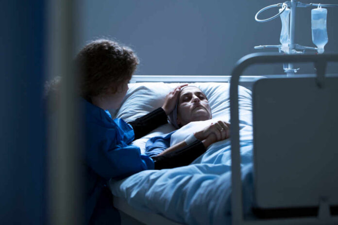 Worried,Caregiver,Supporting,Dying,Woman,With,Cancer,In,The,Hospital Patient in hospital bed comforted by visitor
