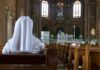 Person in white habit seated in a church pew facing the altar