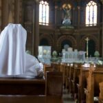 LGBTQ Masses Spark Diocese Standoff Person in white habit seated in a church pew facing the altar