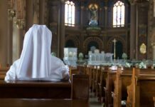 Person in white habit seated in a church pew facing the altar