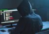 Person in hoodie at dual monitors with code
