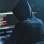 Person in hoodie at dual monitors with code