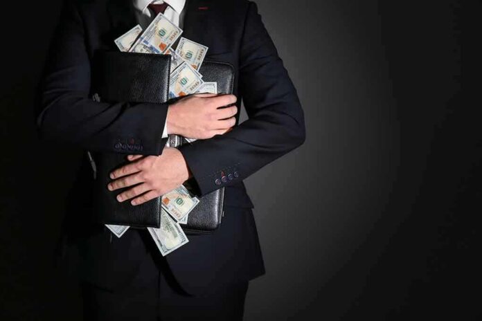shutterstock_1312870373 Businessman hugging briefcase stuffed with cash
