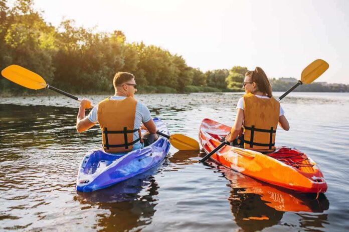 shutterstock_1446108104 Two kayakers paddling on a calm lake at sunset