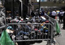 Unvetted Shelter Dump Near Brooklyn Schools? A crowded street with individuals sitting behind barriers and bags, highlighting urban homelessness