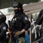 Riot police in tactical gear stand guard outside a building