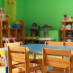 Brightly colored classroom with wooden tables and shelves filled with toys