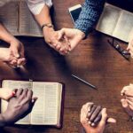 Group holding hands around open books on a wooden table