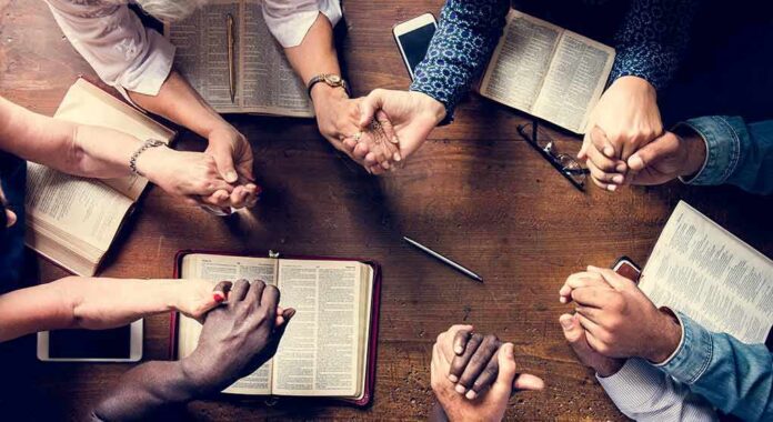shutterstock_1081710347 Group holding hands around open books on a wooden table