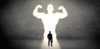 Businessman with briefcase casts a large muscular shadow on wall