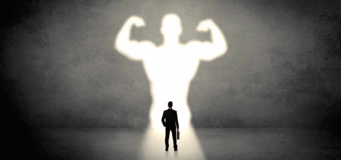shutterstock_1094388167 Businessman with briefcase casts a large muscular shadow on wall