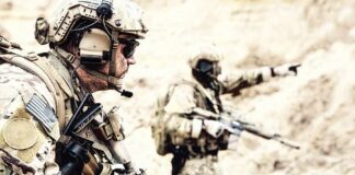 Soldiers in camouflage gear with rifles in a sandy terrain