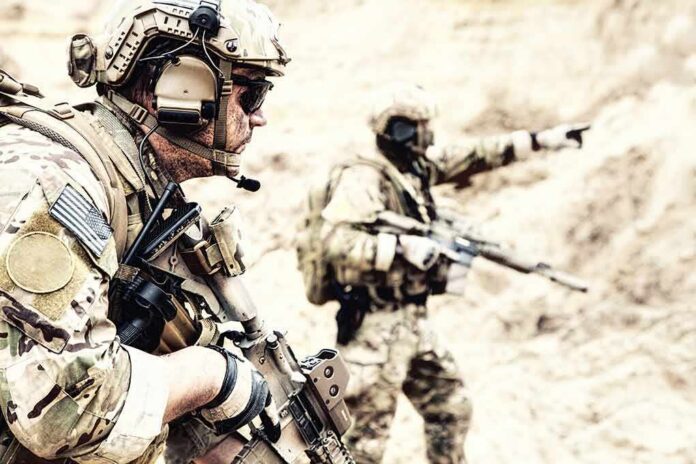 shutterstock_1117495193 Soldiers in camouflage gear with rifles in a sandy terrain