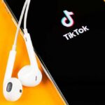 Smartphone with TikTok app and white wired earbuds on yellow background