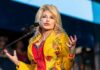 America Pauses: Dolly’s Star Buried In Blooms Singer performing on stage in a bright yellow floral jacket