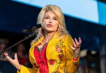 America Pauses: Dolly’s Star Buried In Blooms Singer performing on stage in a bright yellow floral jacket