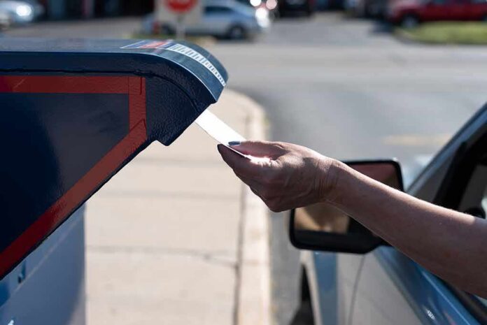 shutterstock_1807712515 Hand mailing an envelope into a blue mailbox