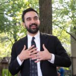 City Grocery Gambit Sparks Immigrant Revolt Man in suit speaking with hands on chest outdoors
