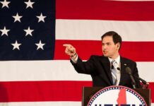 Rubio Drops Hammer On ICC Boss Speaker in suit pointing during speech before large American flag