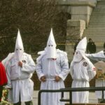 KKK Smear Explodes—Campaign Scrambles ku klux klan members in white robes and hoods at a public gathering