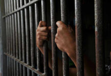 Hands gripping prison cell bars tightly.