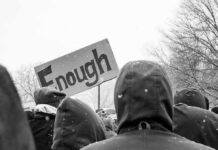 crowd in winter coats at a protest holding a sign