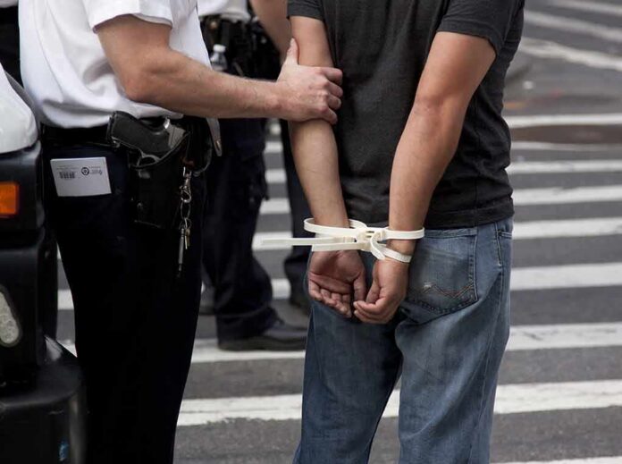 shutterstock_113188777 police officer detains person with hands zip-tied behind back