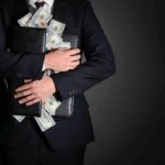 Donor Cash, Lone Rate Hike — Pay-To-Play Stench Shadows Hobbs Businessman hugging briefcase stuffed with cash