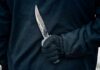 Gloved hand holding a serrated knife against a dark jacket