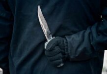Gloved hand holding a serrated knife against a dark jacket