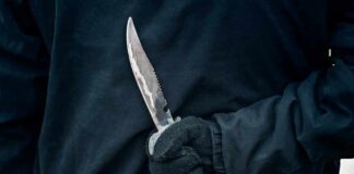 Gloved hand holding a serrated knife against a dark jacket
