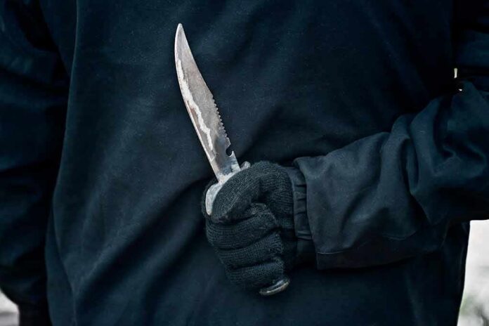 Gloved hand holding a serrated knife against a dark jacket