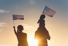 Silhouettes of a family waving American flags at sunset