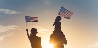 Silhouettes of a family waving American flags at sunset